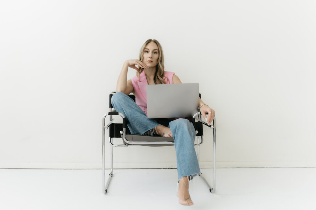 A female entrepreneur sitting with an open laptop in a minimalist modern chair, looking poised and ready for business.